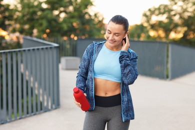 Photo of Young woman with earphones and bottle of water before running outdoors