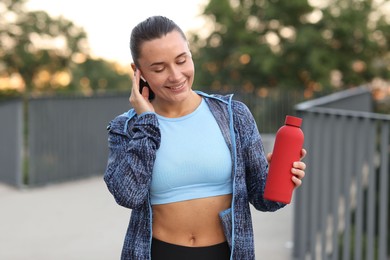 Photo of Young woman with earphones and bottle of water before running outdoors