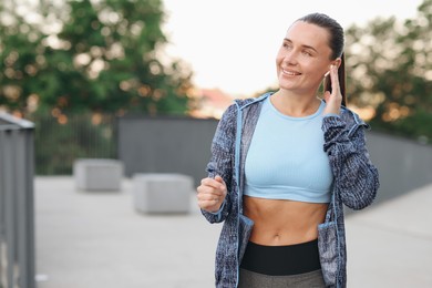 Photo of Young woman with earphones in sportswear before running outdoors, space for text