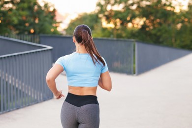 Photo of Young woman in sportswear running outdoors, back view. Space for text
