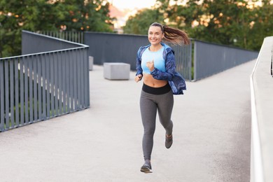 Photo of Athletic young woman in sportswear running outdoors