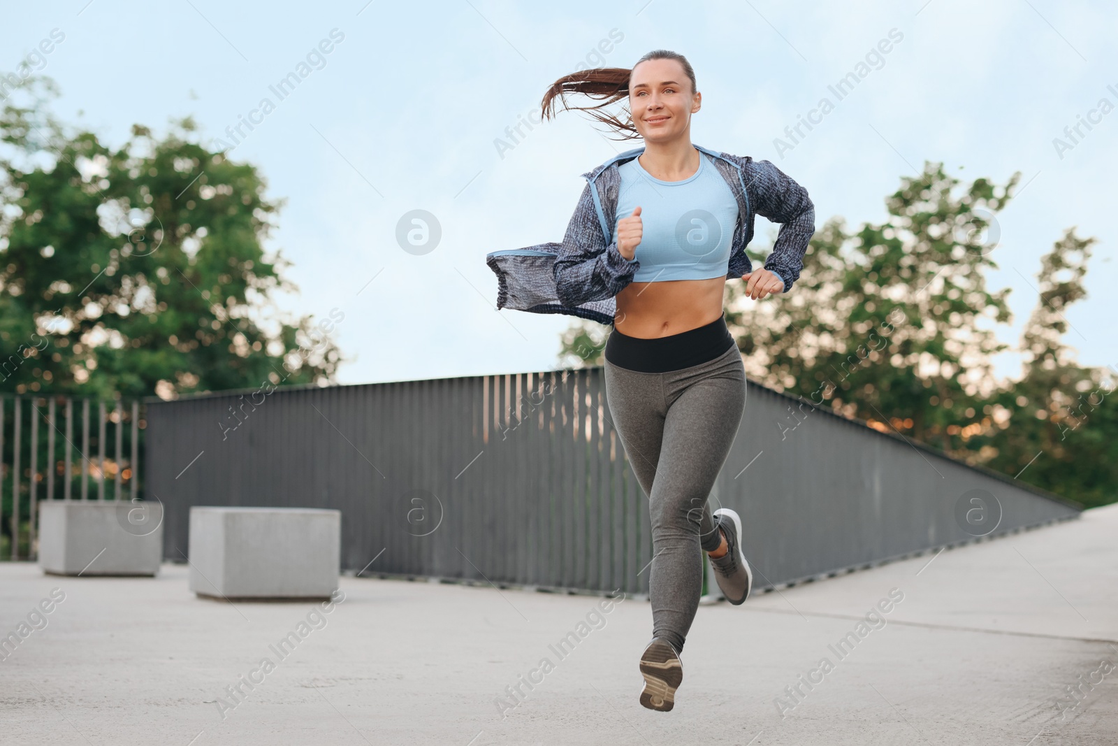 Young woman in sportswear running outdoors, space for text Photo of Young woman in sportswear running outdoors, space for text
