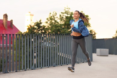 Photo of Young woman in sportswear running outdoors, space for text