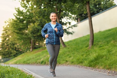 Photo of Young woman in sportswear running outdoors, space for text