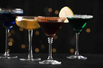 Photo of Different martini cocktails in glasses on black table against blurred lights, closeup