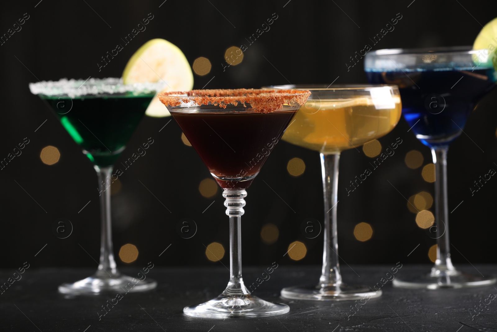 Different martini cocktails in glasses on black table against blurred lights, closeup Photo of Different martini cocktails in glasses on black table against blurred lights, closeup