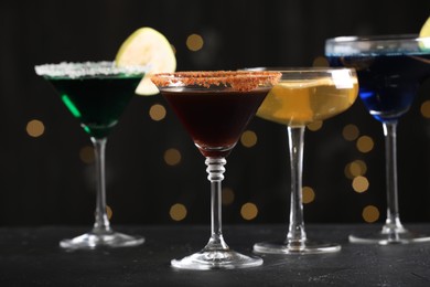 Photo of Different martini cocktails in glasses on black table against blurred lights, closeup