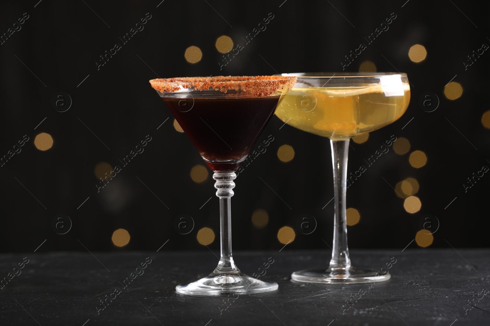 Different martini cocktails in glasses on black table against blurred lights, closeup Photo of Different martini cocktails in glasses on black table against blurred lights, closeup