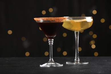 Photo of Different martini cocktails in glasses on black table against blurred lights, closeup