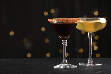 Photo of Different martini cocktails in glasses on black table against blurred lights, closeup. Space for text