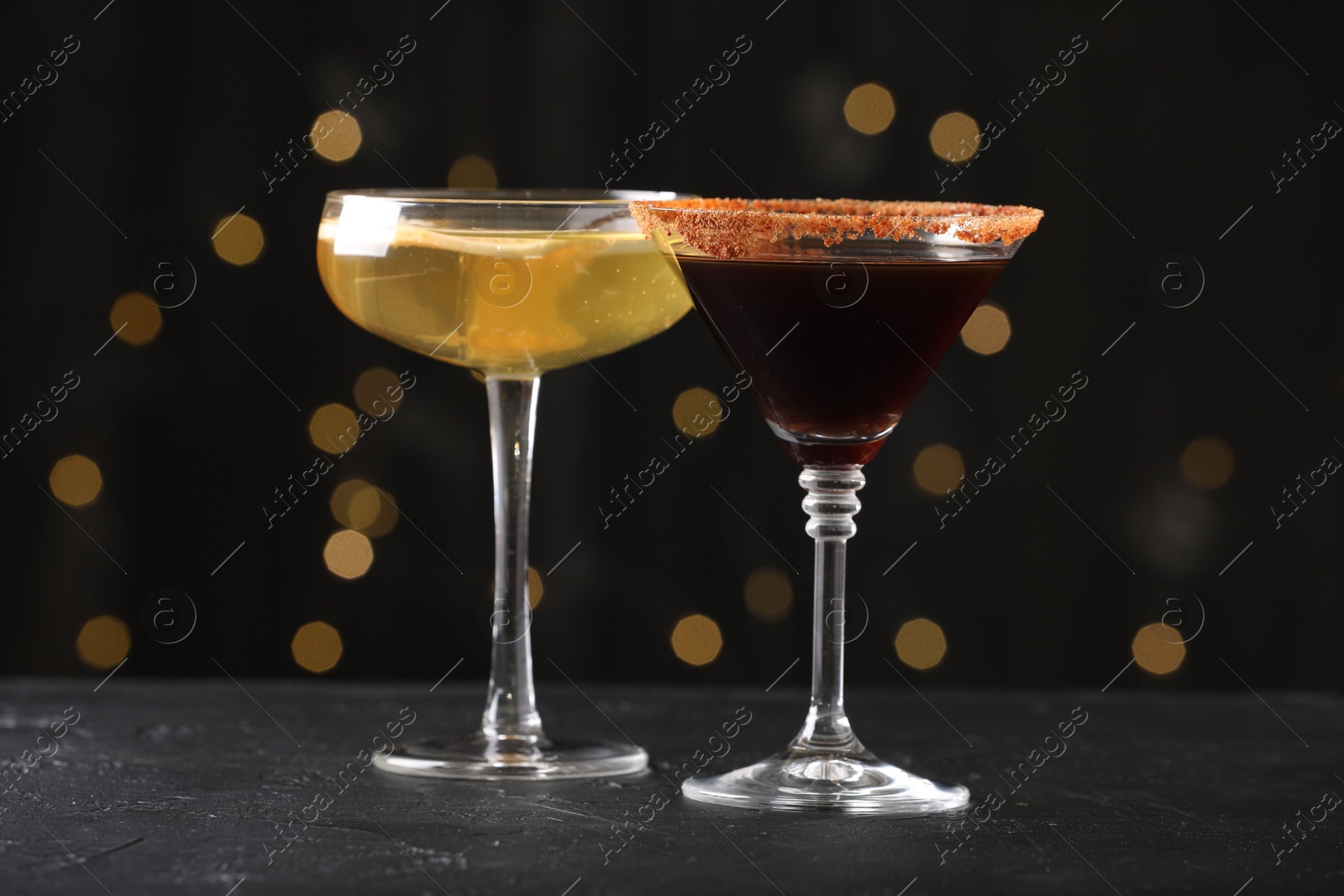 Photo of Different martini cocktails in glasses on black table against blurred lights, closeup