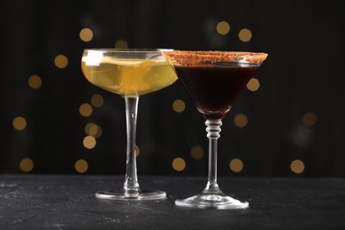Photo of Different martini cocktails in glasses on black table against blurred lights, closeup