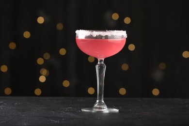 Photo of Martini cocktail with sugar in glass on black table against blurred lights, closeup