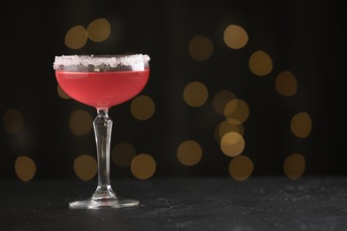 Photo of Martini cocktail with sugar in glass on black table against blurred lights, closeup. Space for text
