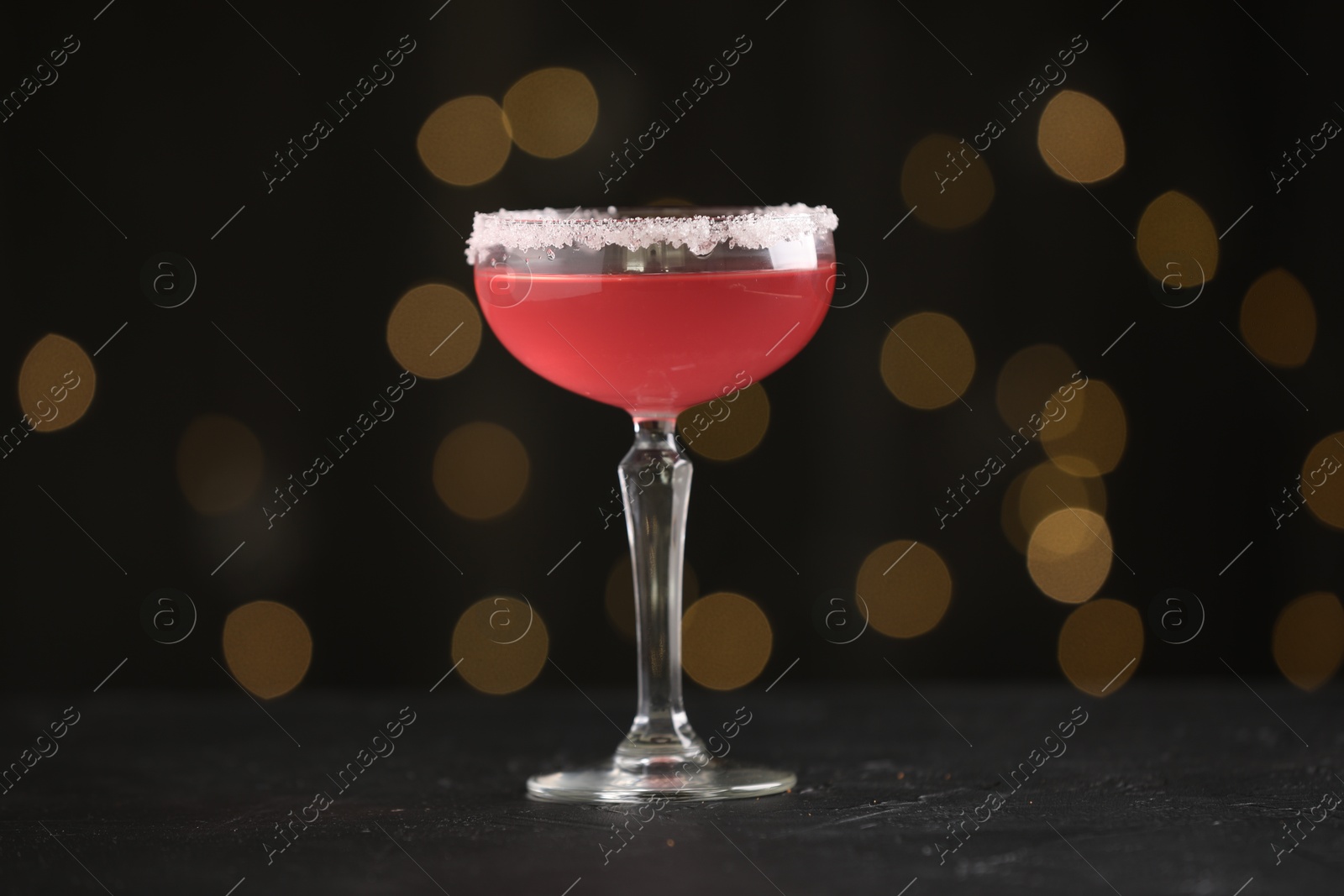 Martini cocktail with sugar in glass on black table against blurred lights, closeup Photo of Martini cocktail with sugar in glass on black table against blurred lights, closeup