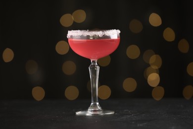 Photo of Martini cocktail with sugar in glass on black table against blurred lights, closeup