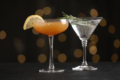 Photo of Different martini cocktails in glasses on black table against blurred lights, closeup