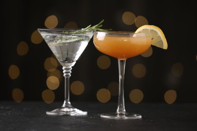 Photo of Different martini cocktails in glasses on black table against blurred lights, closeup