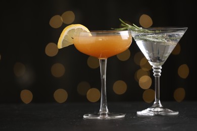 Photo of Different martini cocktails in glasses on black table against blurred lights, closeup. Space for text