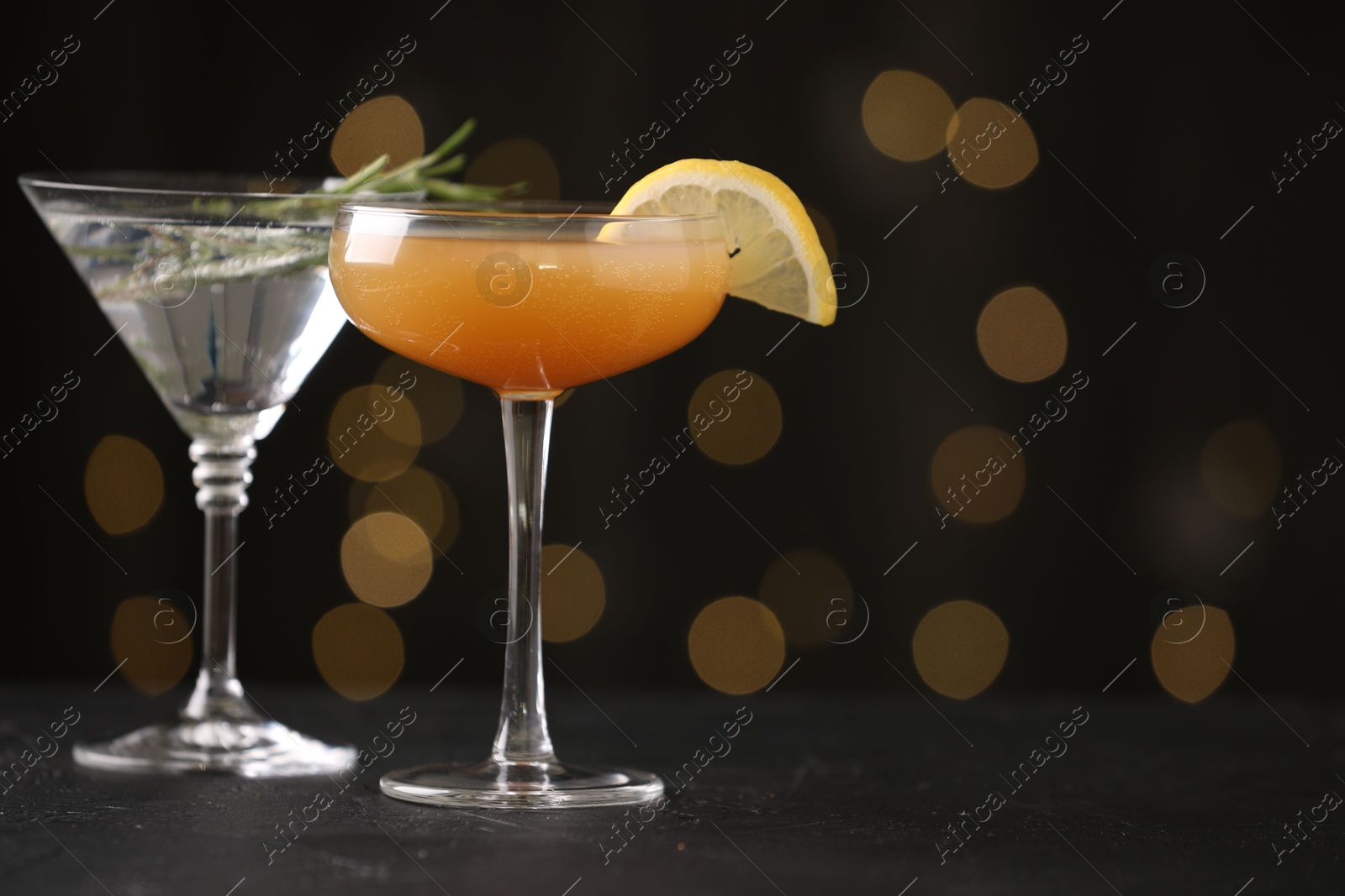 Different martini cocktails in glasses on black table against blurred lights, closeup. Space for text Photo of Different martini cocktails in glasses on black table against blurred lights, closeup. Space for text