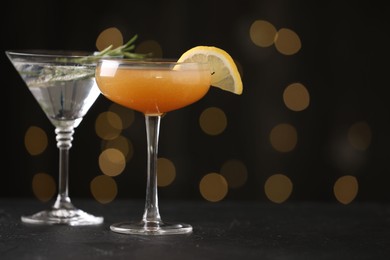 Photo of Different martini cocktails in glasses on black table against blurred lights, closeup. Space for text