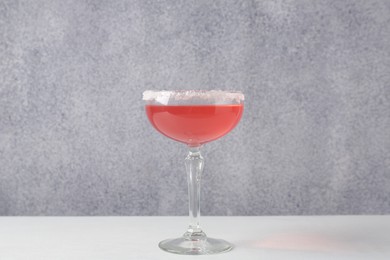 Photo of Martini cocktail with sugar in glass on white table near grey wall, closeup