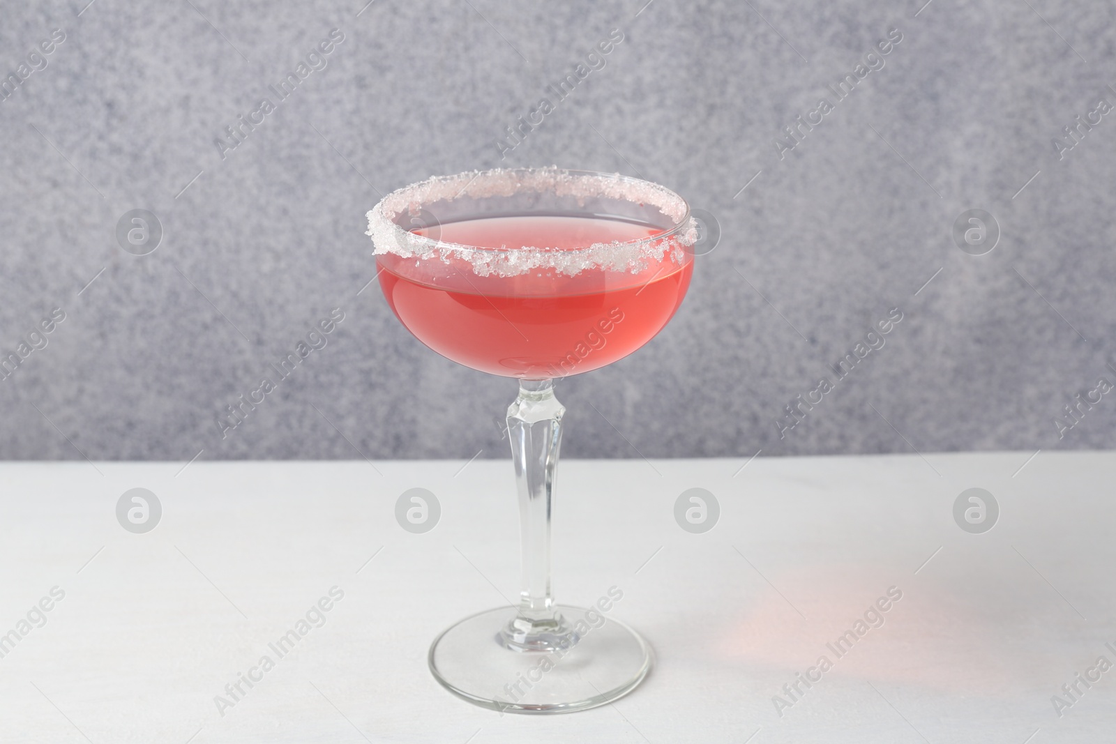 Martini cocktail with sugar in glass on white table near grey wall, closeup Photo of Martini cocktail with sugar in glass on white table near grey wall, closeup