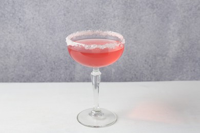 Photo of Martini cocktail with sugar in glass on white table near grey wall, closeup