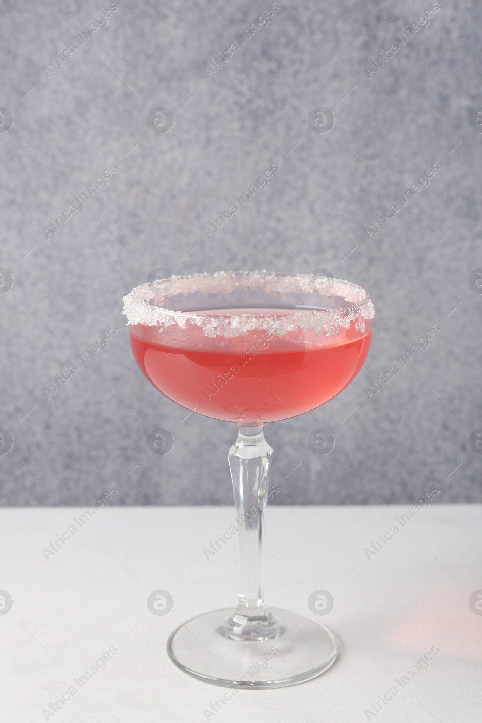 Martini cocktail with sugar in glass on white table near grey wall Photo of Martini cocktail with sugar in glass on white table near grey wall