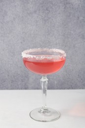 Photo of Martini cocktail with sugar in glass on white table near grey wall