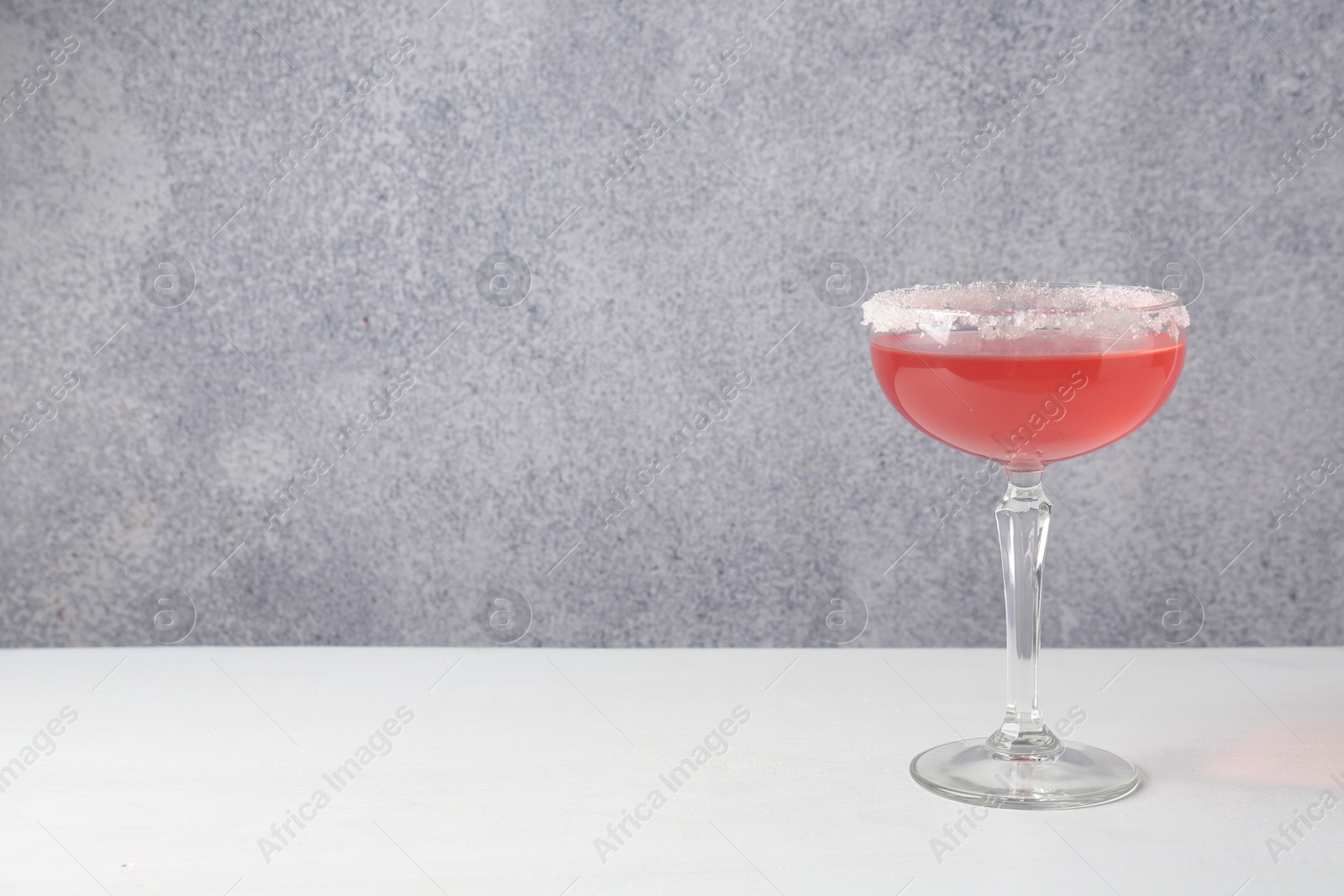 Martini cocktail with sugar in glass on white table near grey wall. Space for text Photo of Martini cocktail with sugar in glass on white table near grey wall. Space for text