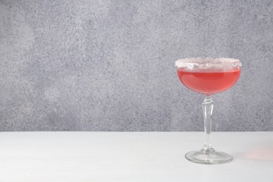 Photo of Martini cocktail with sugar in glass on white table near grey wall. Space for text