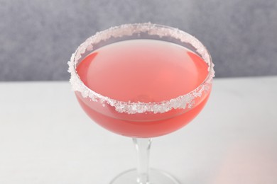 Photo of Martini cocktail with sugar in glass on white table near grey wall, closeup