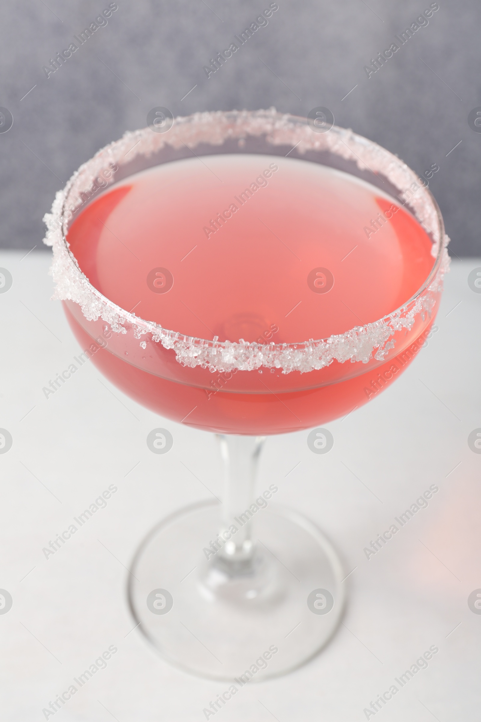 Martini cocktail with sugar in glass on white table near grey wall, closeup Photo of Martini cocktail with sugar in glass on white table near grey wall, closeup