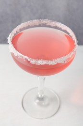 Photo of Martini cocktail with sugar in glass on white table near grey wall, closeup