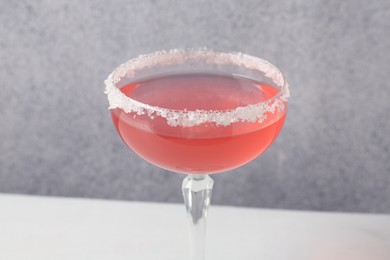 Photo of Martini cocktail with sugar in glass on white table near grey wall, closeup