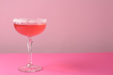 Photo of Martini cocktail with sugar in glass on pink background, closeup. Space for text