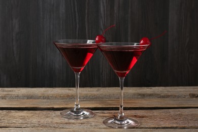 Photo of Martini cocktail with cherries in glasses on wooden table, closeup