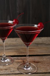 Photo of Martini cocktail with cherries in glasses on wooden table, closeup
