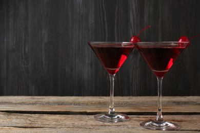 Photo of Martini cocktail with cherries in glasses on wooden table, closeup. Space for text
