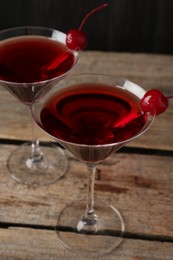 Photo of Martini cocktail with cherries in glasses on wooden table, closeup