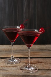 Photo of Martini cocktail with cherries in glasses on wooden table, closeup