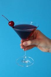 Photo of Woman holding martini cocktail with cherry in glass on light blue background, closeup