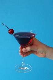Photo of Woman holding martini cocktail with cherry in glass on light blue background, closeup