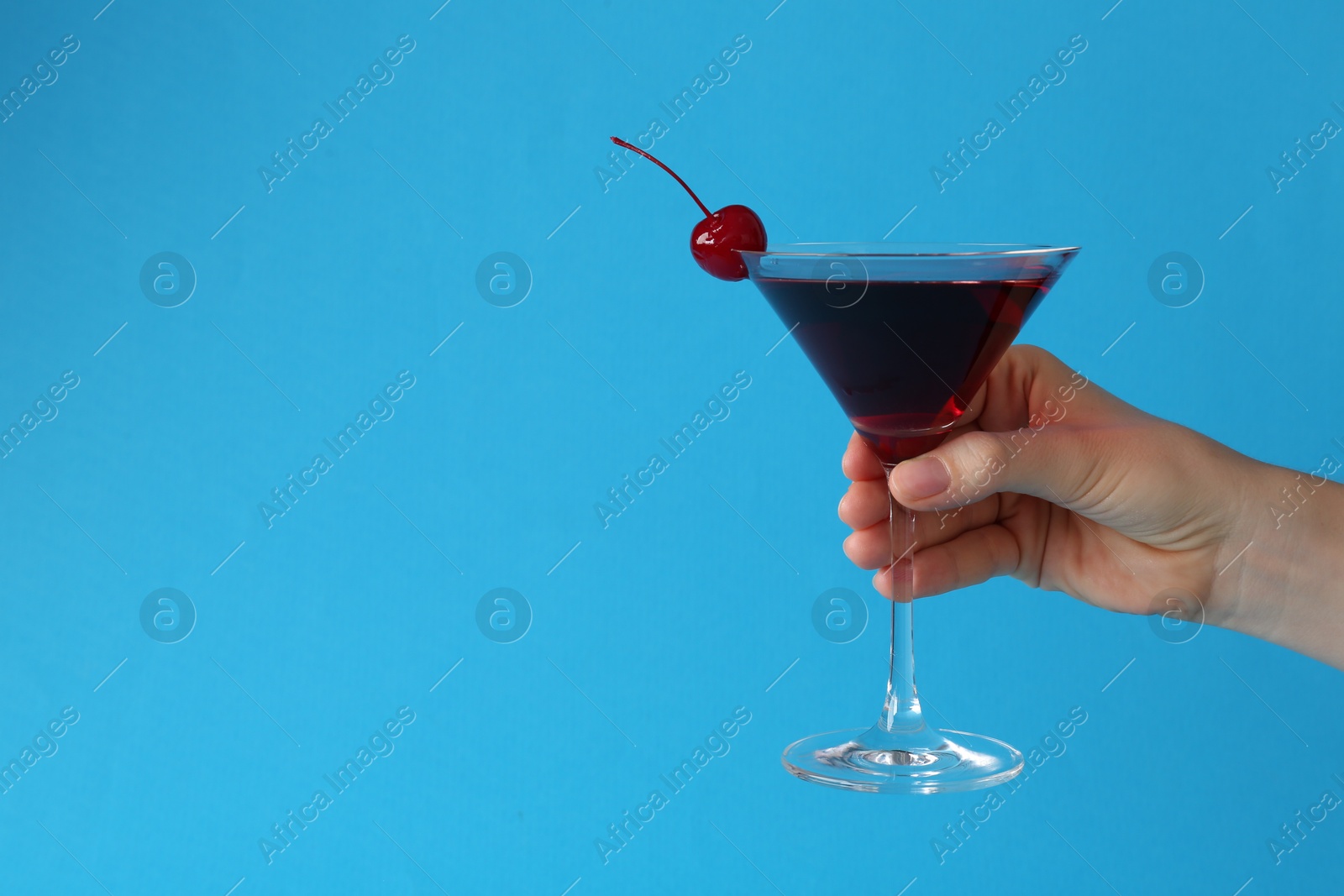 Woman holding martini cocktail with cherry in glass on light blue background, closeup. Space for text Photo of Woman holding martini cocktail with cherry in glass on light blue background, closeup. Space for text