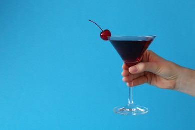Photo of Woman holding martini cocktail with cherry in glass on light blue background, closeup. Space for text