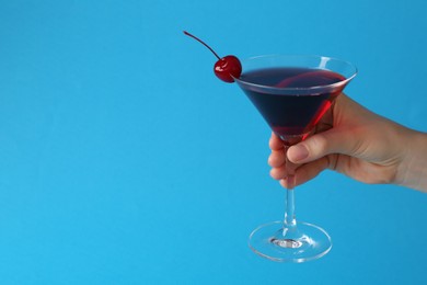 Photo of Woman holding martini cocktail with cherry in glass on light blue background, closeup. Space for text