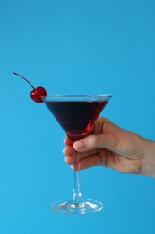 Photo of Woman holding martini cocktail with cherry in glass on light blue background, closeup