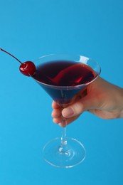 Photo of Woman holding martini cocktail with cherry in glass on light blue background, closeup