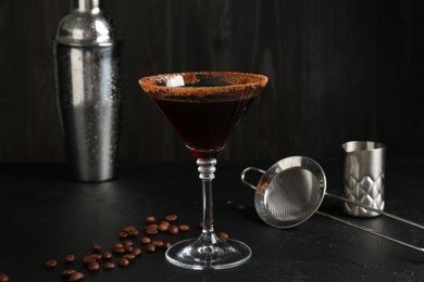 Photo of Martini cocktail with sugar in glass, coffee beans and shaker on black table, closeup